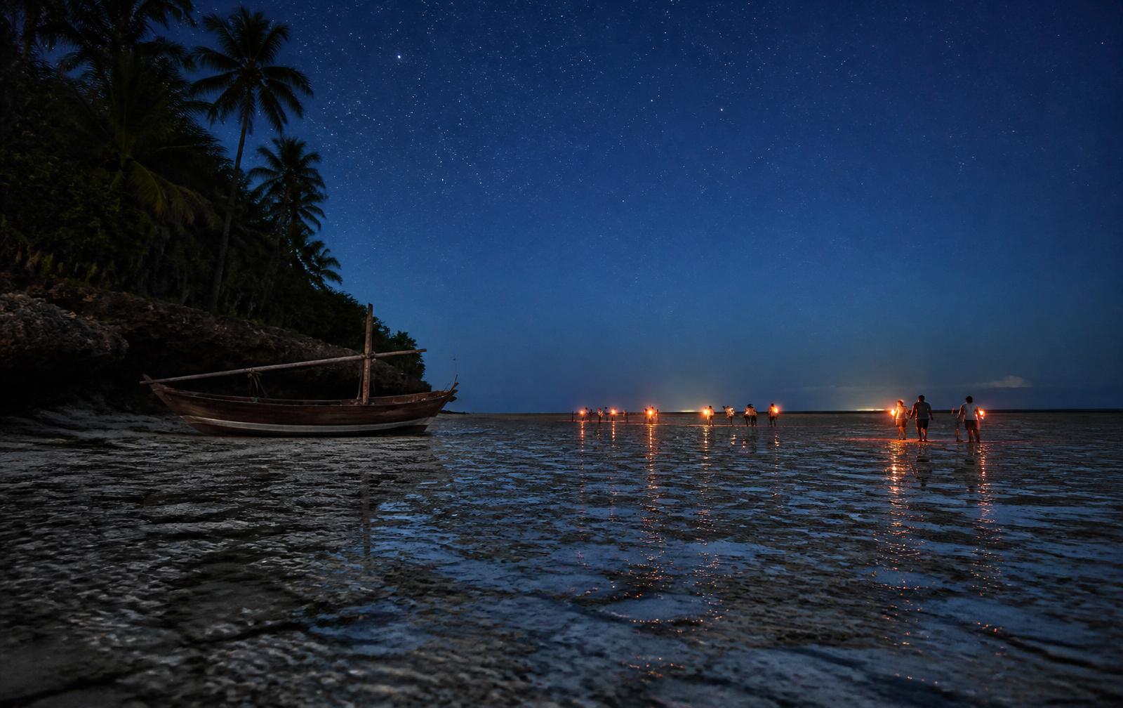 Torch lights of a small group walking on the exposed ocean bed at night in Zanzibar