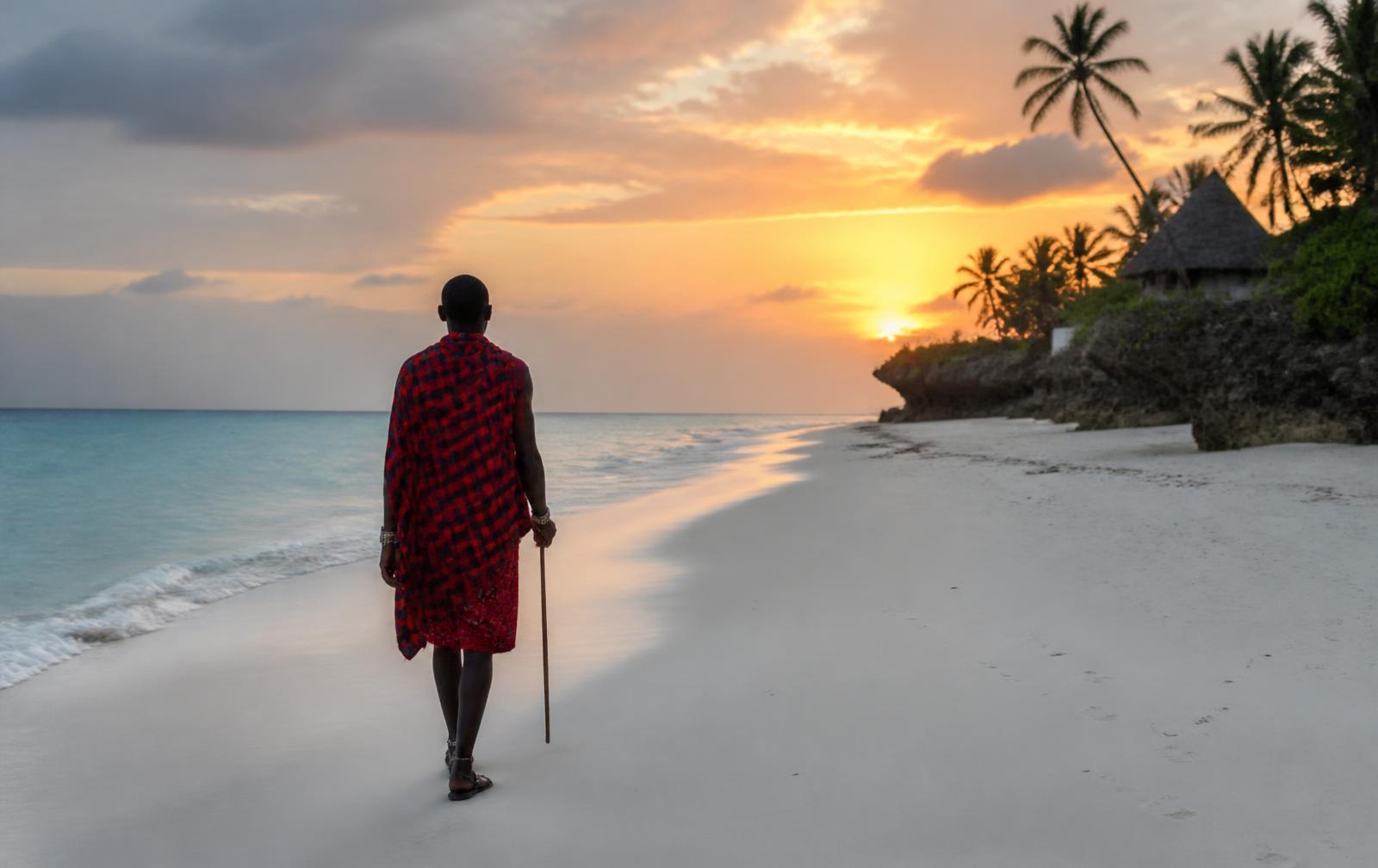 Maasai man in traditional dress walking along a Zanzibar beach at sunset
